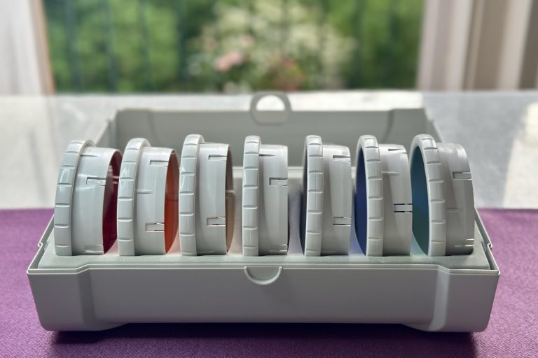Sieben Bioptron-Farbaufsätze in der Box vor dem Tageslicht – das volle Farbspektrum für die individuelle Lichttherapie