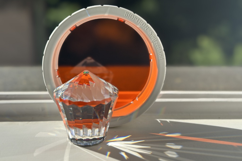 Bioptron-Farbaufsatz Orange im Sonnenlicht mit Kristall — sichtbare prismatische Lichtstrahlen am Fensterbrett zeigen die Lichtwirkung