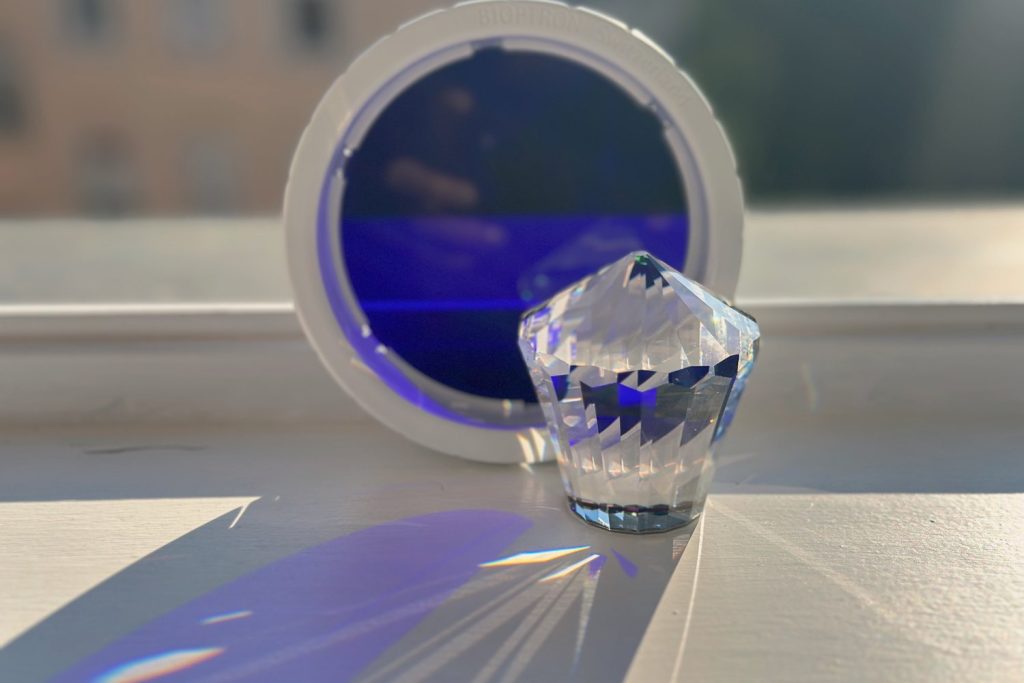 Bioptron-Indigo-Aufsatz mit Bleikristall vor dem Fenster – das Lichtspektrum bricht sich auf der Fensterbank