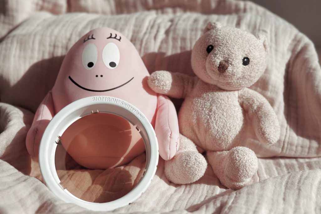 Bioptron-Aufsatz zwischen Barbapapa-Figur und Teddybär – die Lampe als Teil der Kinderwelt