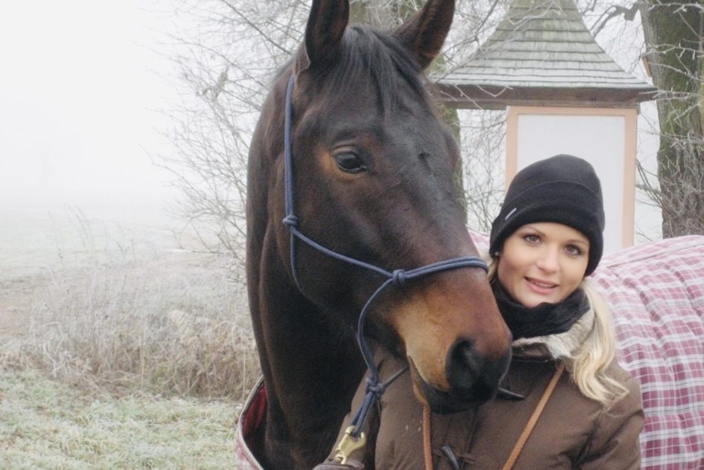 Andrea Viehauser steht neben ihrem braunen Pferd Rogno auf einem nebligen Feldweg im Winter