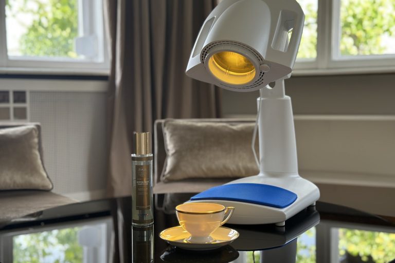Bioptron PRO 1 auf einem Glastisch im Wohnzimmer, daneben das Hyperlight Fluid Fusion Spray — die Lichttherapie-Lampe in einem ruhigen häuslichen Setting.