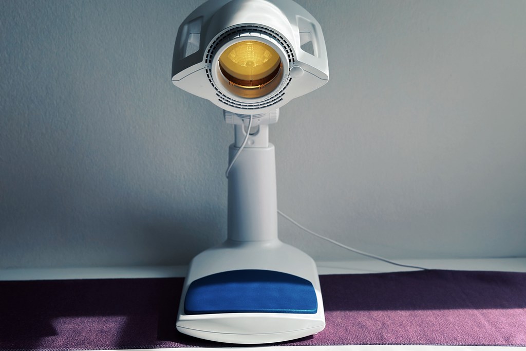 Bioptron PRO 1 mit eingeschaltetem warmem Licht und gelbem Farbaufsatz, frontal aufgenommen — typische Anwendungsposition der Lichttherapie-Lampe.