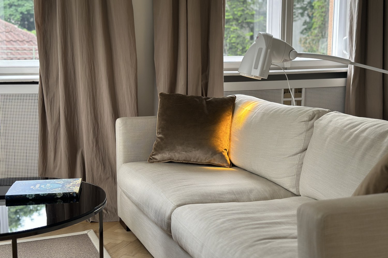 Bioptron-Lampe auf einem hellen Sofa mit samtigem Kissen — der warme Lichtkegel der Lampe fällt auf das Kissen und schafft eine ruhige Atmosphäre für die Lichttherapie zu Hause.