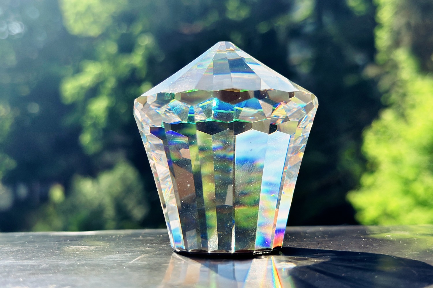 Geschliffener Kristall in Sonnenlicht mit Regenbogenfarben vor grünem Bokeh – Symbol für polychromatisches Licht und Lichtspektrum