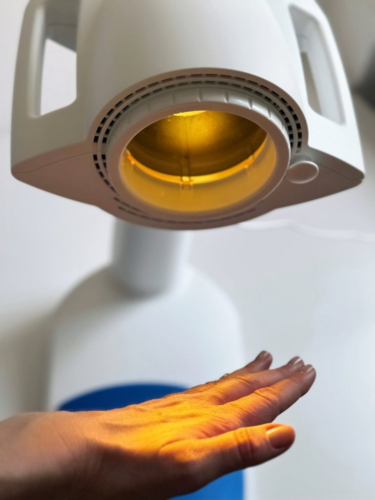 Hand unter der Bioptron-Lampe mit gelbem Farbaufsatz – das hyperpolarisierte Licht trifft direkt auf die Haut