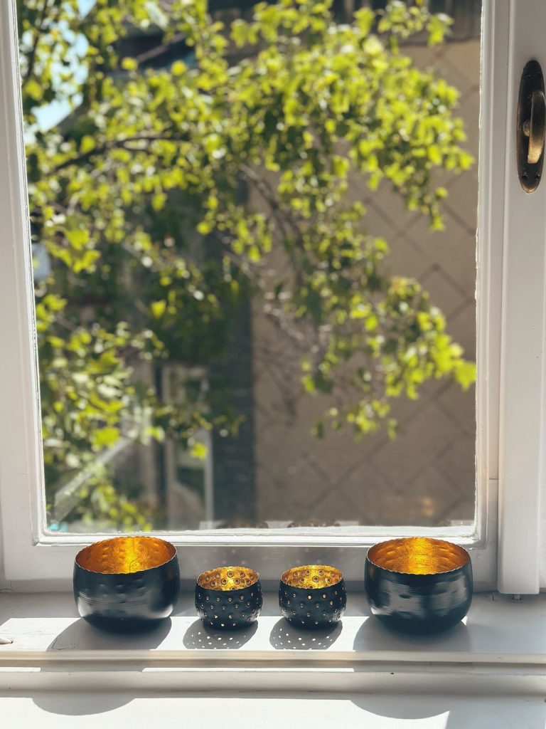 Schwarz-goldene Teelichthalter am sonnigen Fensterbrett – Sinnbild für Licht, das von innen leuchtet