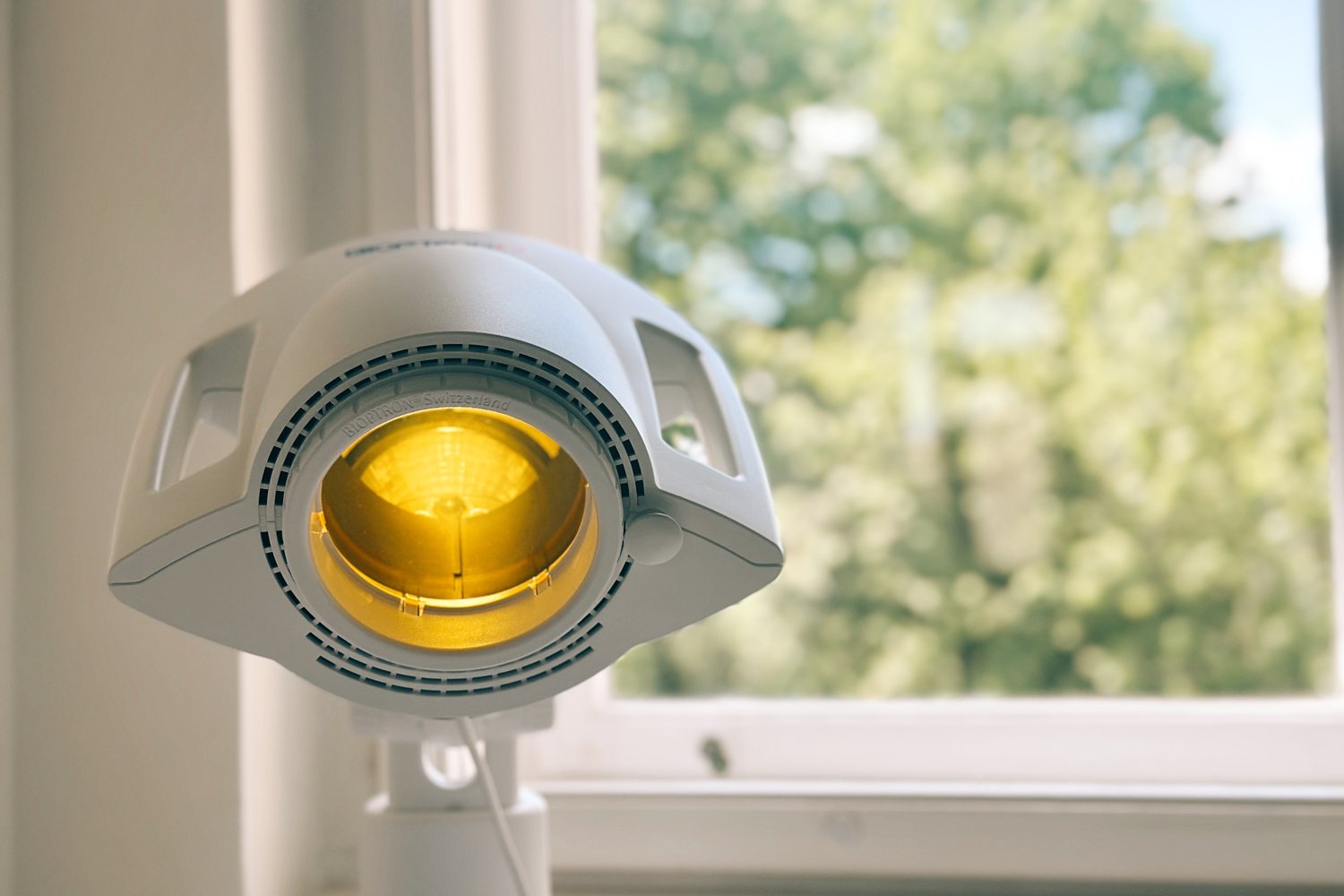 Bioptron PRO 1 mit gelbem Farbaufsatz vor dem Fenster im Tageslicht – die Lampe wartet auf die nächste Anwendung
