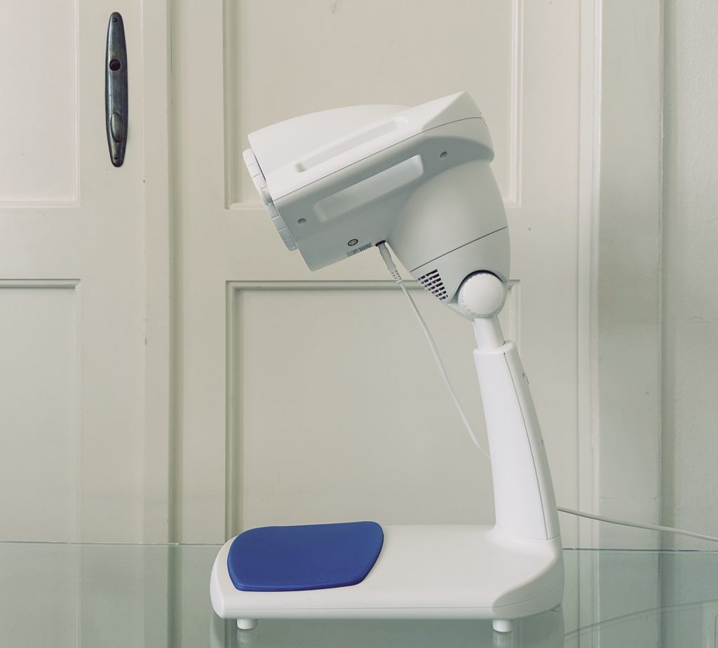 Bioptron PRO1 mit Tischstativ und blauer Akzentplatte – Detailaufnahme der Schweizer Lichttherapielampe