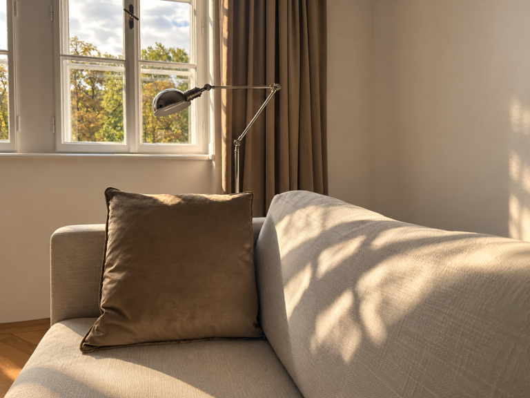 Gemütliches Sofa mit Kissen vor einem Fenster mit Blick auf herbstliche Bäume, warmes Nachmittagslicht