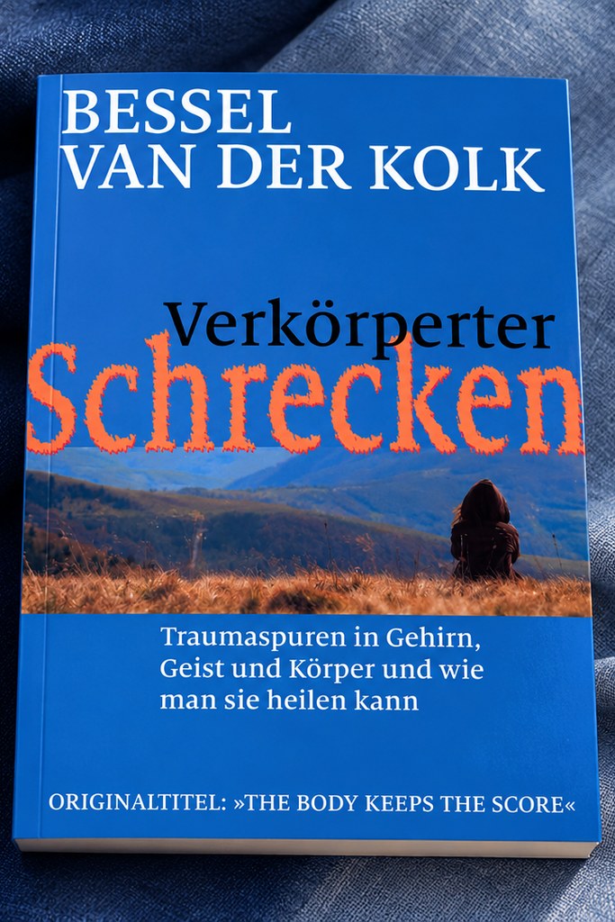 Das Taschenbuch „Verkörperter Schrecken — Traumaspuren in Gehirn, Geist und Körper und wie man sie heilen kann" von Bessel van der Kolk mit blauem Cover und einer Person in herbstlicher Hügellandschaft, liegend auf blauem Leinenstoff.